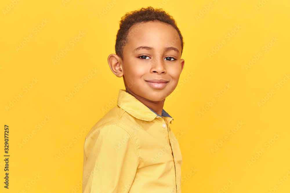 Happy childhood concept. Close up shot of handsome friendly looking boy in yellow shirt smiling, being in good mood posing isolated against blank background with copy space for your information Happy childhood concept. Close up shot of handsome friendly looking boy in yellow shirt smiling, being in good mood posing isolated against blank background with copy space for your information