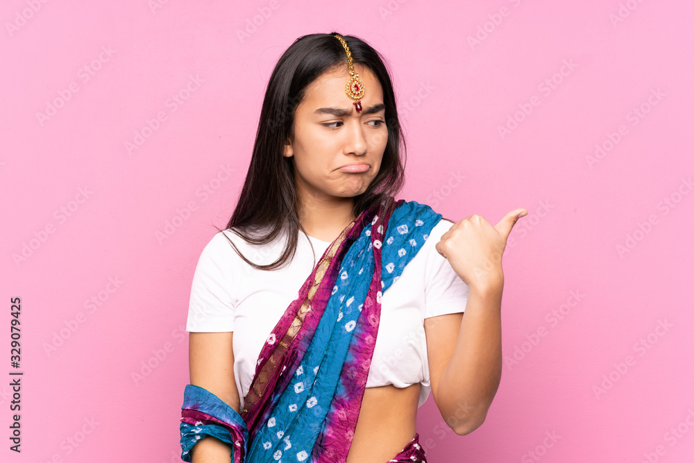 Young Indian woman with sari over isolated background unhappy and pointing to the side Young Indian woman with sari over isolated background unhappy and pointing to the side