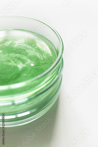 Transparent green shampoo or facial cleaner in glass petri dish on white background with selective focus, above. Concept natural organic cosmetic