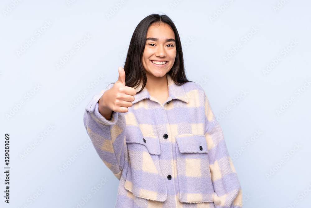 Young Indian woman isolated on blue background with thumbs up because something good has happened Young Indian woman isolated on blue background with thumbs up because something good has happened