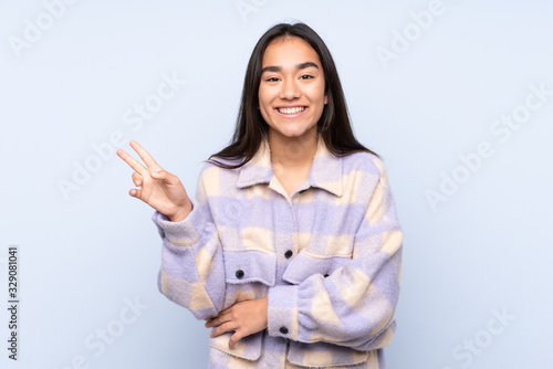 Young Indian woman isolated on blue background smiling and showing victory sign