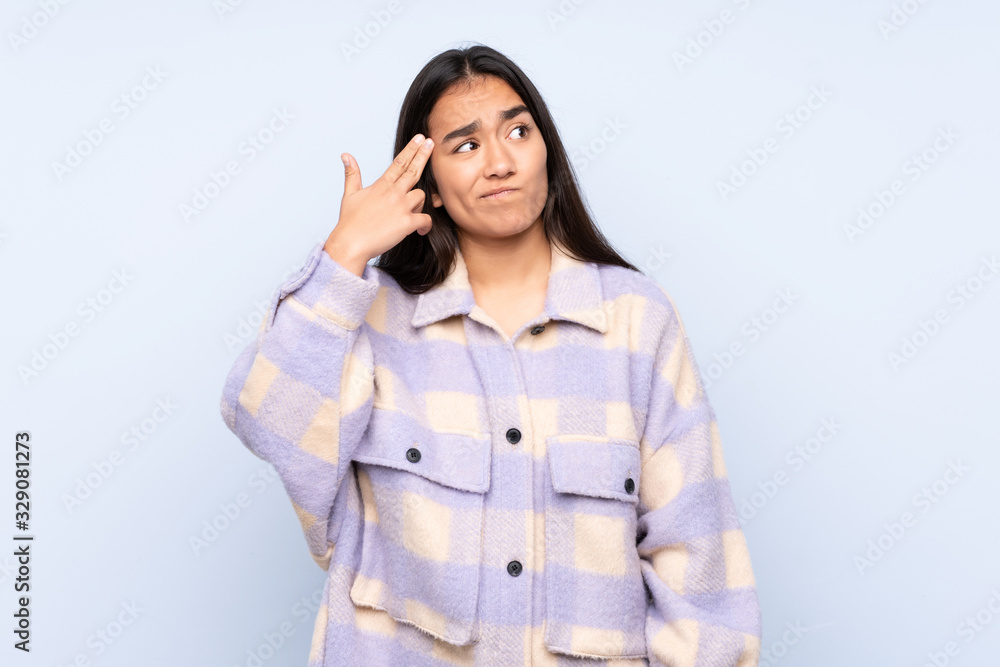 Young Indian woman isolated on blue background with problems making suicide gesture Young Indian woman isolated on blue background with problems making suicide gesture