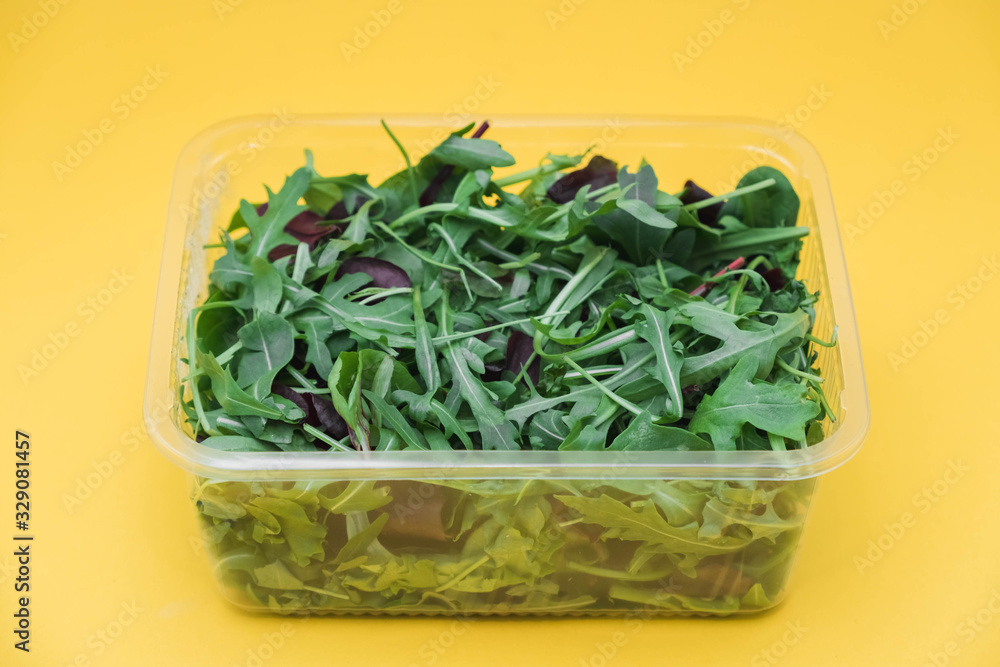 Fresh leaves of arugula, lettuce, spinach, beets for salad in a plastic plate on a yellow background. Copy, empty space for text Fresh leaves of arugula, lettuce, spinach, beets for salad in a plastic plate on a yellow background. Copy, empty space for text