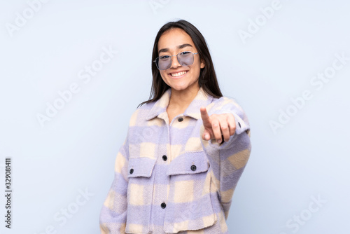 Young Indian woman isolated on blue background points finger at you with a confident expression © luismolinero
