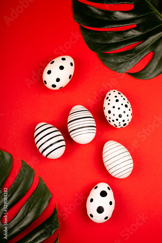 Creative graphic eggs with green tropical leaves on bright red background. Easter concept. Vertical photo.