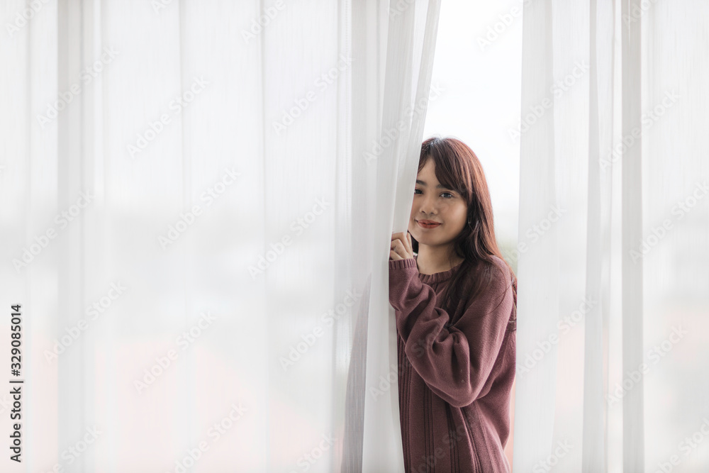 Portrait of beautiful young Asian woman wake up in morning break with freshness and standing near the window and opening white curtains. Portrait of beautiful young Asian woman wake up in morning break with freshness and standing near the window and opening white curtains.