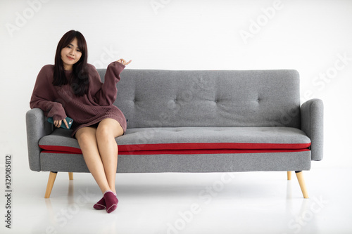 Portrait of beautiful young Asian woman is sitting on sofa and pointing finger to empty. © amornchaijj