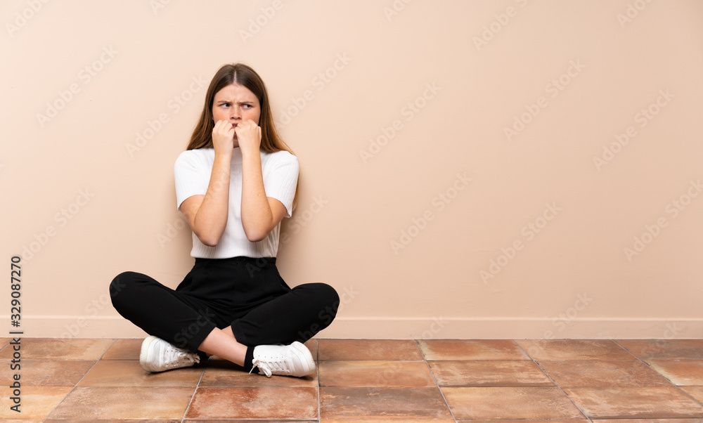 Ukrainian teenager girl sitting on the floor nervous and scared putting hands to mouth Ukrainian teenager girl sitting on the floor nervous and scared putting hands to mouth