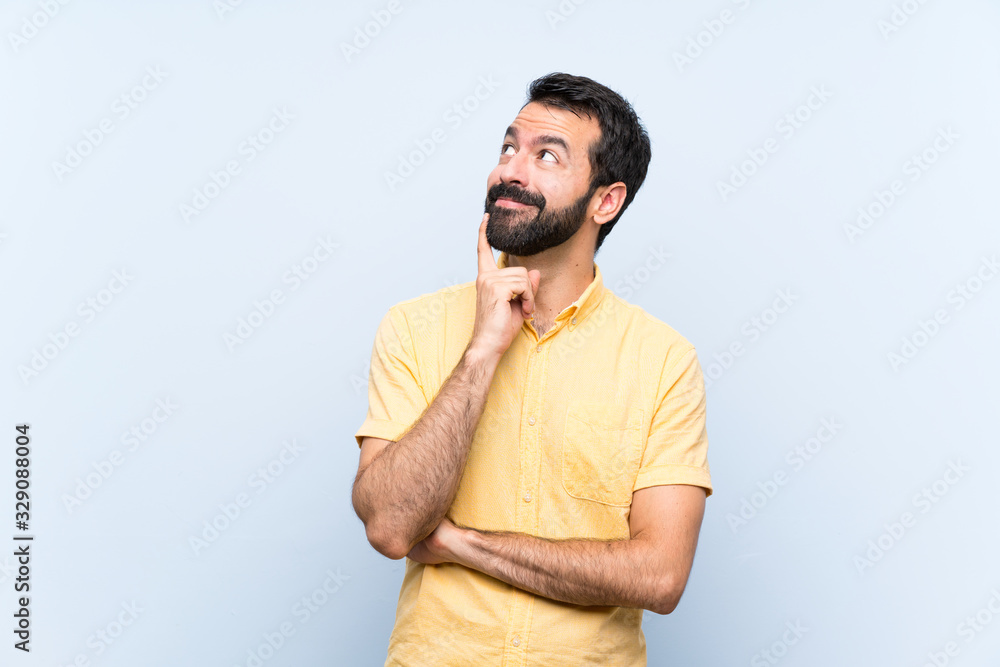 Young man with beard over isolated blue background thinking an idea while looking up Young man with beard over isolated blue background thinking an idea while looking up