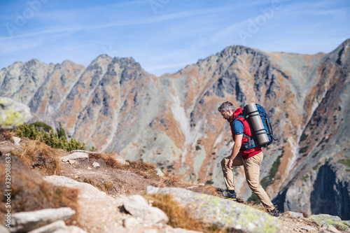 Mature man with backpack hiking in mountains in summer.
