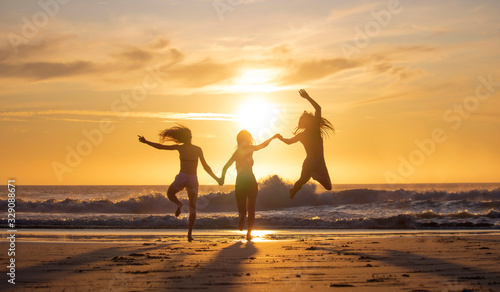 Silhouette of three beautiful women having fun running and jumping on a beach at sunset or sunrise.