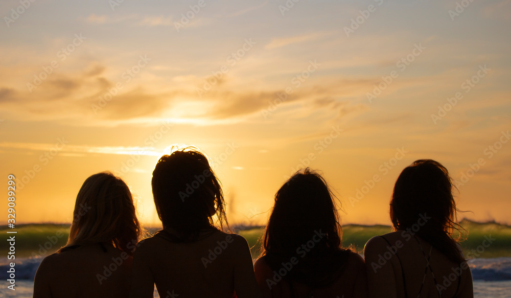 Silhouette of four beautiful women overlooking a beautiful sunrise or sunset view over the ocean.