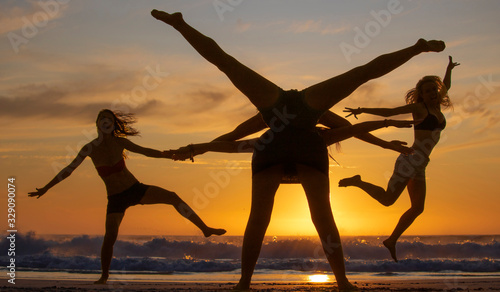 Silhouette of four beautiful women having fun creating shapes at sunset or sunrise on a beach.