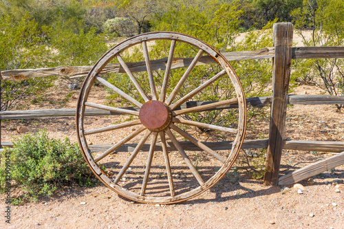 An old wagon wheel leans against a wooden fence in the desert
