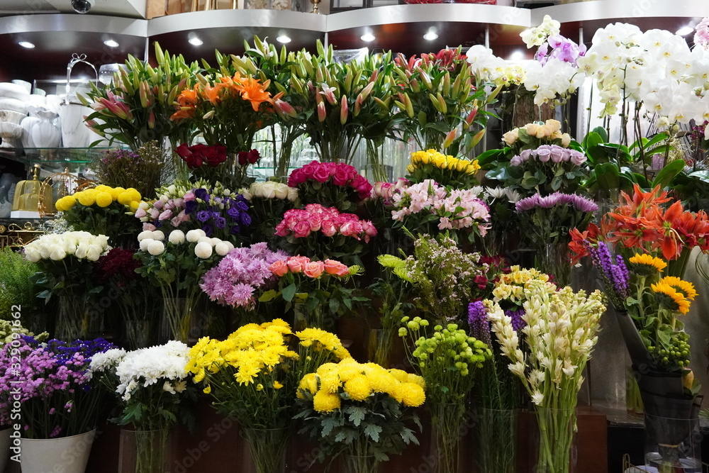 Bouquet of colorful roses and other different flowers at the entry to flower shop at farmers' market. Colorful peony, roses etc. Pots with flowers on the shelf of plant shop. Dubai UAE December 2019