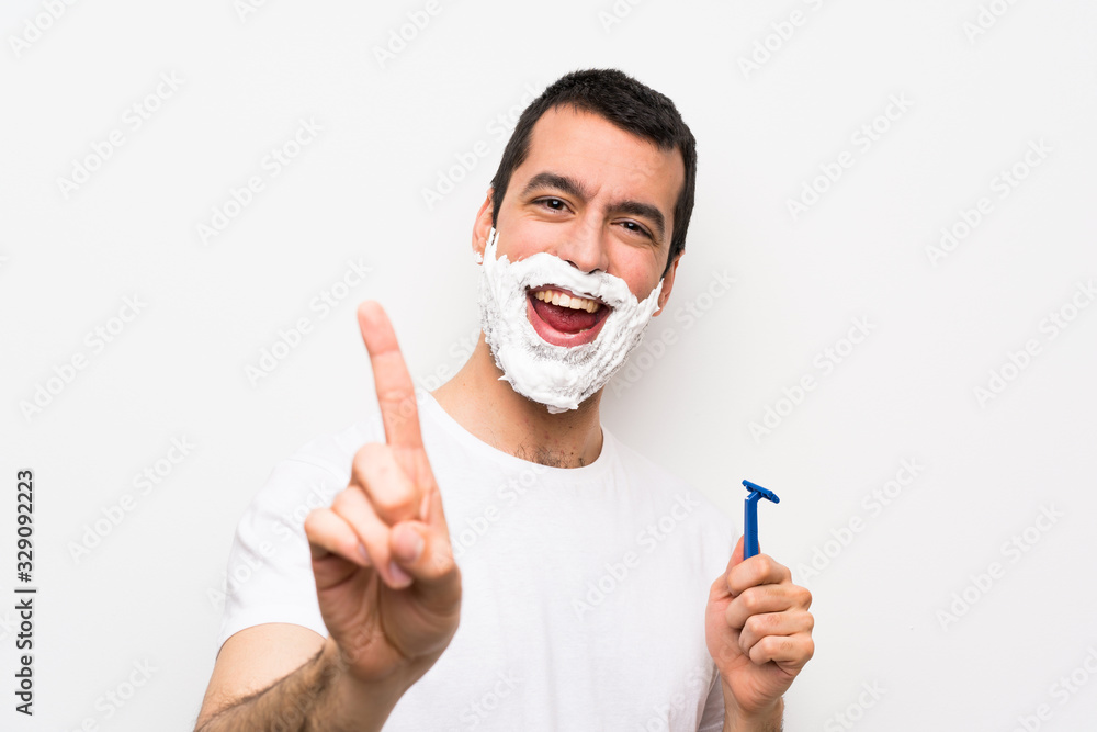 Man shaving his beard over isolated white background showing and lifting a finger