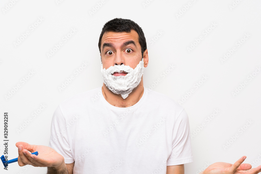 Man shaving his beard over isolated white background making doubts gesture