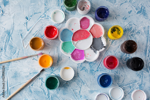 Gouache for drawing different colors with brushes on a gray texture background. Gouache cans are randomly located. Background gray textural brush strokes