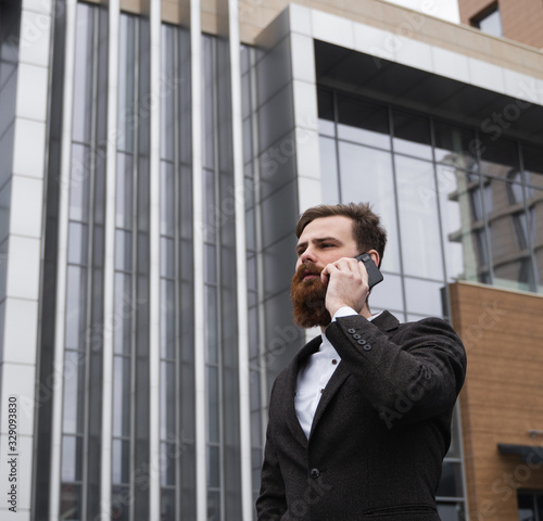 Businessman talking on the phone in financial district. Portrait of a Young urban professional man using smart phone over office building. Business man talking on his smartphone outdoors. Technology.