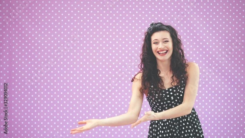 Lovely young girl with kinky hair, in black polka-dots dress dancing, waving comically her hands, pointing at copy space for text or product. photo