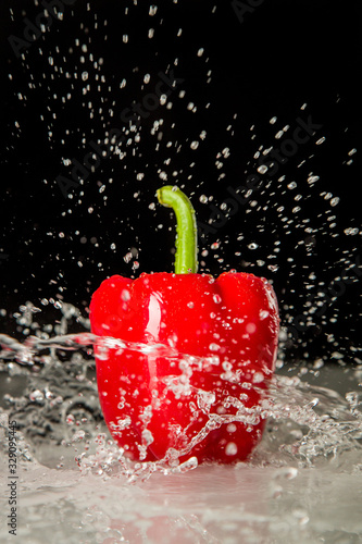Delicious fresh red pepper on dark background getting splashed with water. 