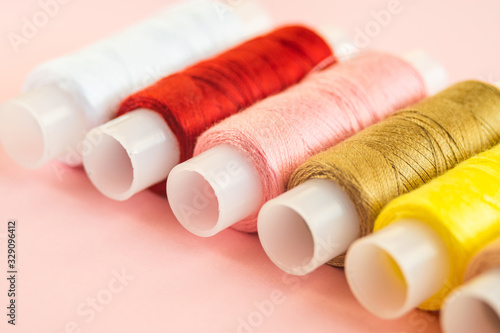 Sewing supplies and accessories for needlework Multicolored thread coils for sewing clothes on pink background.