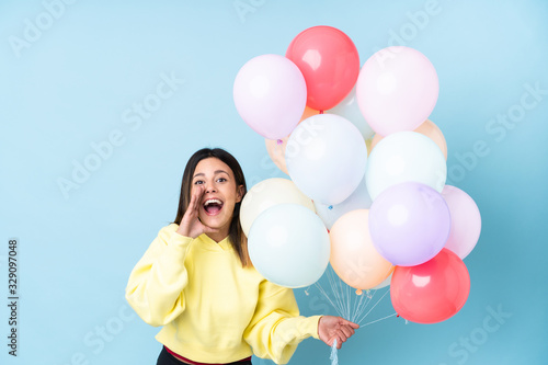 Woman holding balloons in a party over isolated blue background shouting with mouth wide open