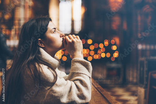 Fototapeta A young woman is sitting with her hands folded and is praying in a church