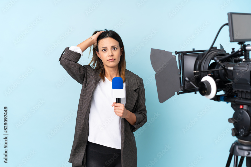 Reporter woman holding a microphone and reporting news over isolated blue background with surprise facial expression