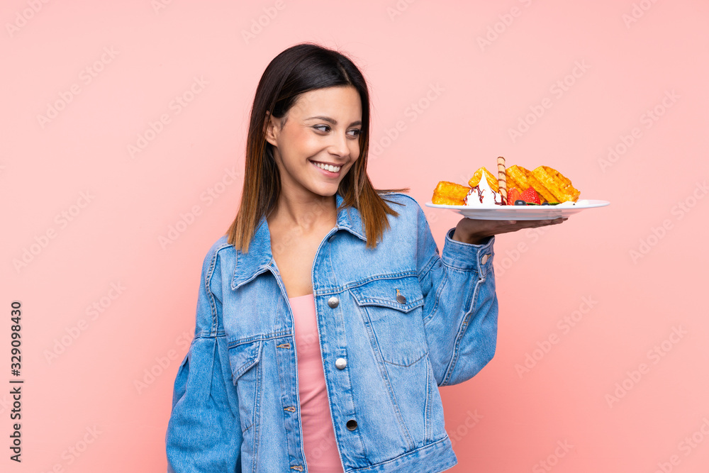 Brunette woman holding waffles over isolated pink background with happy expression Brunette woman holding waffles over isolated pink background with happy expression