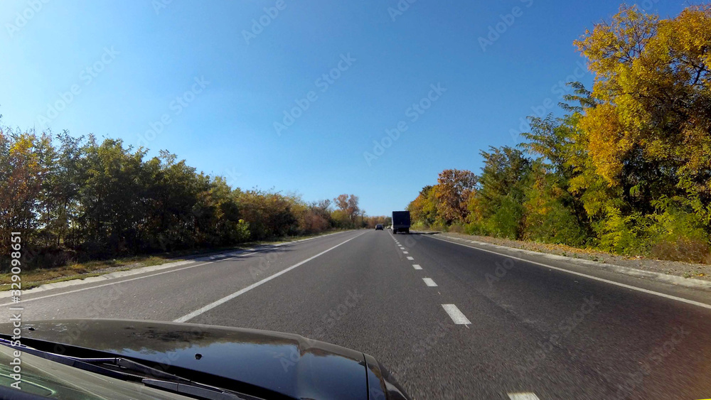 Country highway with a marking sunny autumn day, along the road trees with bright foliage