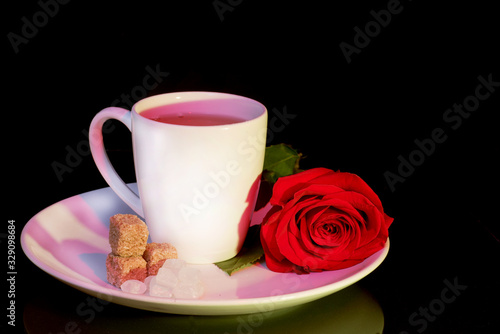 Mug with saucer and sugar and a rose on a black background