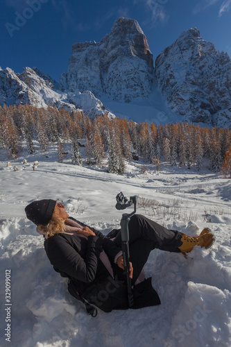 Woman lying in the snow doing a selfie with the phone, Dolomites, Italy. Concept: technology, happy people surrounded by nature, happy people on vacation