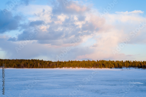 Dramatic sky above the snow-covered frozen Kuito lake, coniferous forest in the background. Winter sunset. Karelia North, Lapland photo