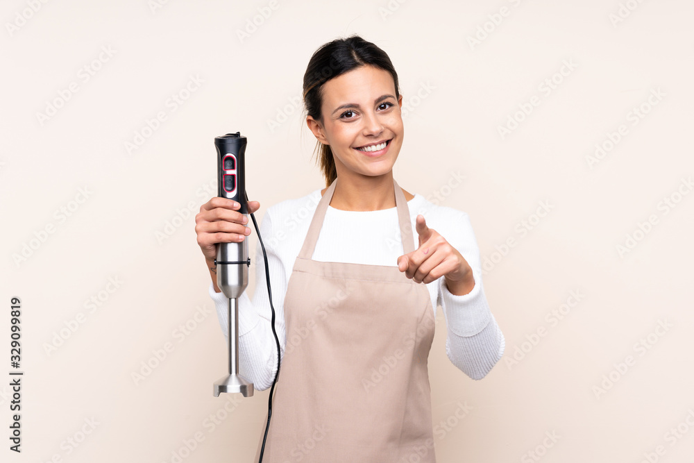 Woman using hand blender over isolated background points finger at you with a confident expression Woman using hand blender over isolated background points finger at you with a confident expression