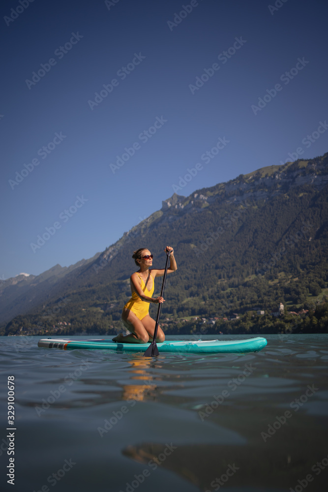 Pretty, young woman paddling on a paddle board on a lake, enjoying a lovely summer day