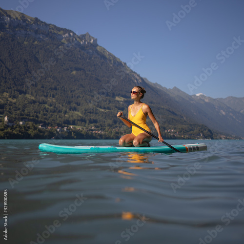 Pretty, young woman paddling on a paddle board on a lake, enjoying a lovely summer day