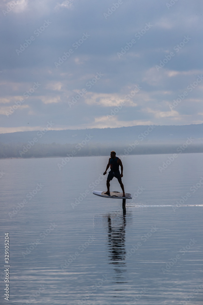 Man riding an electric hydrofoil foil board on a lake with a life jacket