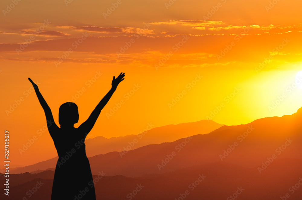 Silhouette of a girl with her hands raised up against the background of the sunset in the mountains