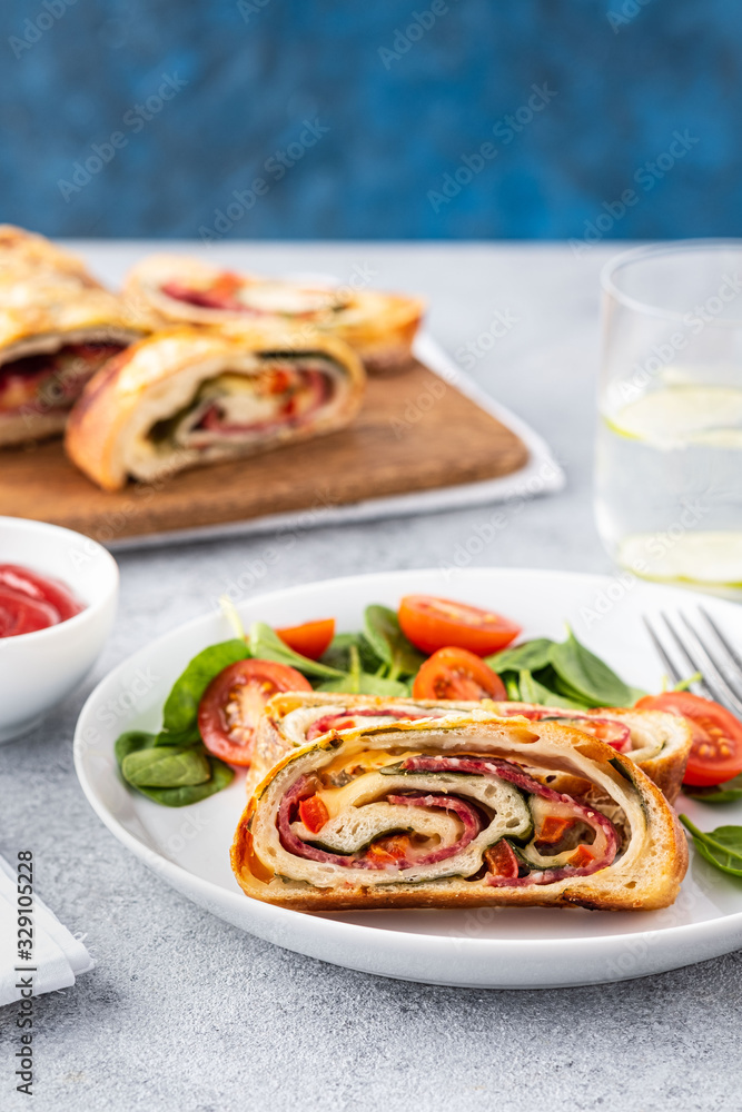 Italian food Pizza roll stromboli with cheese, salami, spinach and red pepper a light background. Italian food Pizza roll stromboli with cheese, salami, spinach and red pepper a light background.