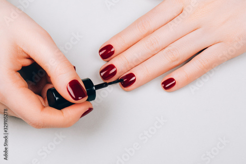 Woman making red manicure by herself on grey background.