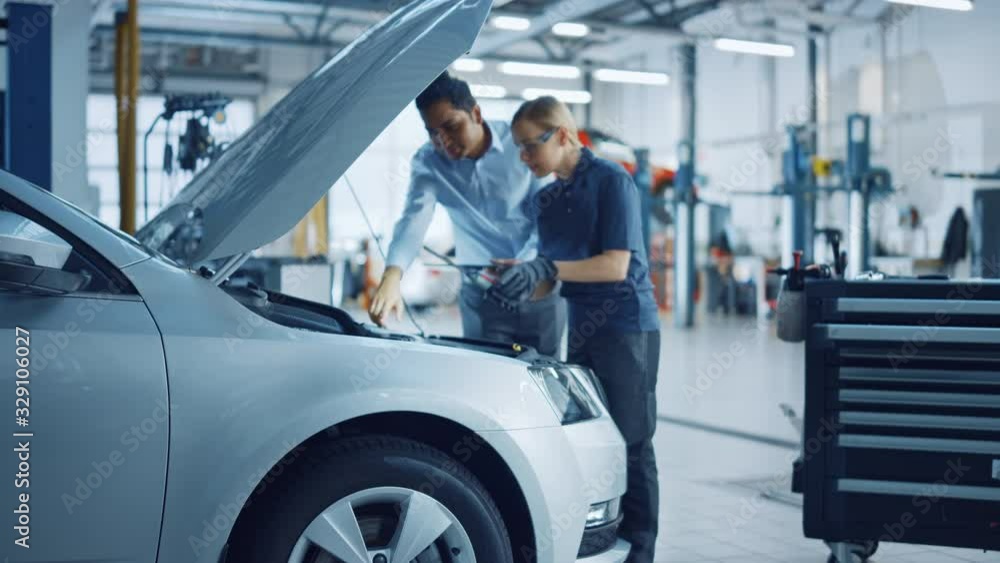 Manager Checks Data on a Tablet and Explains an Engine Breakdown to an Empowering Female Mechanic. Car Service Employees Inspect a Car with Internal Combustion Engine. Modern Clean Workshop. Manager Checks Data on a Tablet and Explains an Engine Breakdown to an Empowering Female Mechanic. Car Service Employees Inspect a Car with Internal Combustion Engine. Modern Clean Workshop.