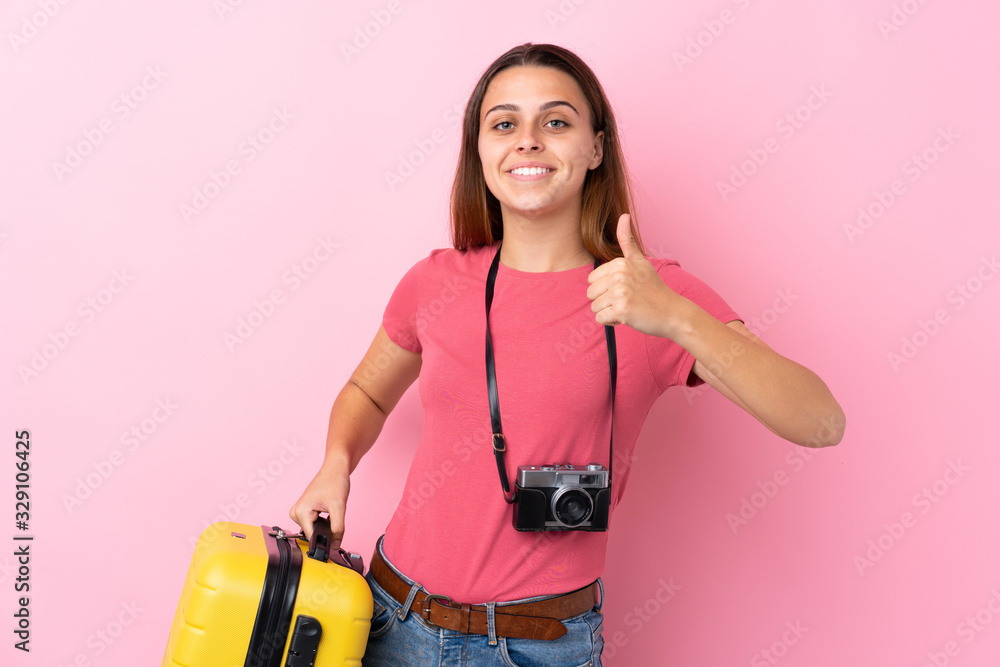 Teenager traveler girl holding a suitcase over isolated pink background with thumbs up because something good has happened