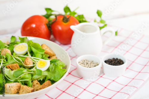 Fresh vegetable salad with fresh tomato  cucumber  lettuce  spinach  egg on plate topping with biscuits. There is a dressing in the small cup. Healty food concept