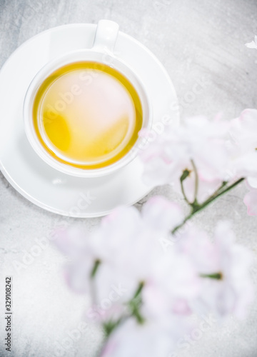 Asian teacup with green japan tea. Blossoming branches flowers around on gray table.