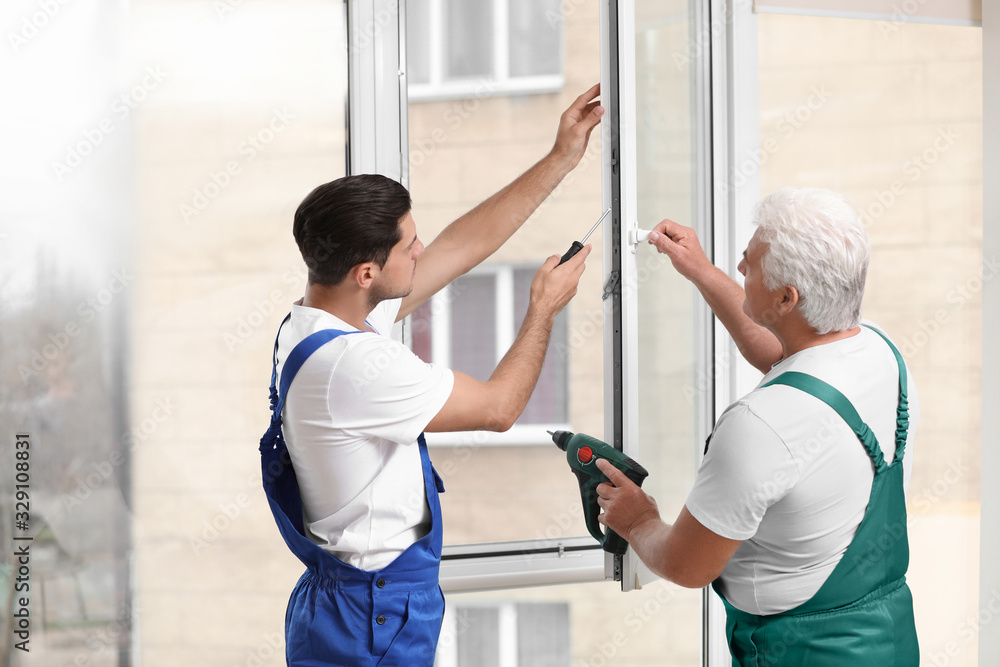 Fototapeta premium Construction workers repairing plastic window with screwdriver indoors