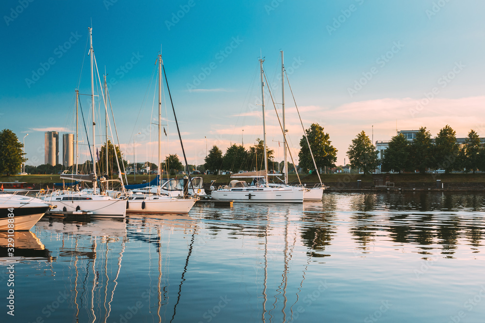 Riga, Latvia. Pleasure boats and Yachts Moored At The City Pier Harbour Bay And Quay In Summer Sunny Evening. Reflections From Boats In Water Of Western Dvina River