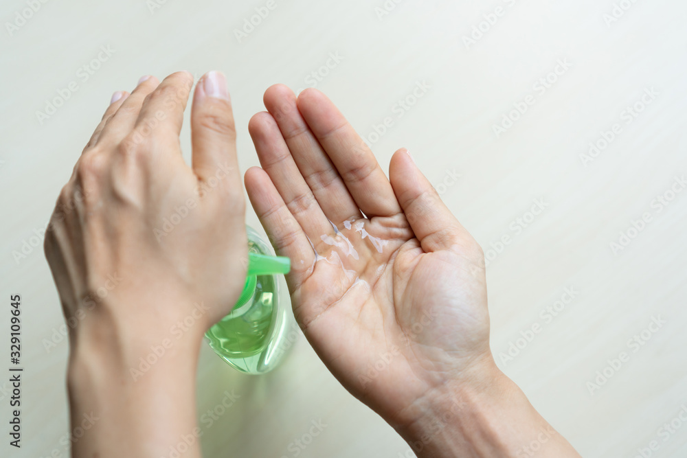 Fototapeta premium Woman applying sanitizer gel onto her hand for protection against infectious virus, bacteria and germs in wooden background. Protection concept.
