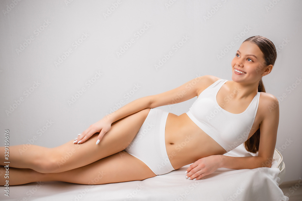 attractive slim lady with perfect body after laser epilation procedure in salon. attractive lady lie on bed after beauty procedures, look side and smile. white background attractive slim lady with perfect body after laser epilation procedure in salon. attractive lady lie on bed after beauty procedures, look side and smile. white background