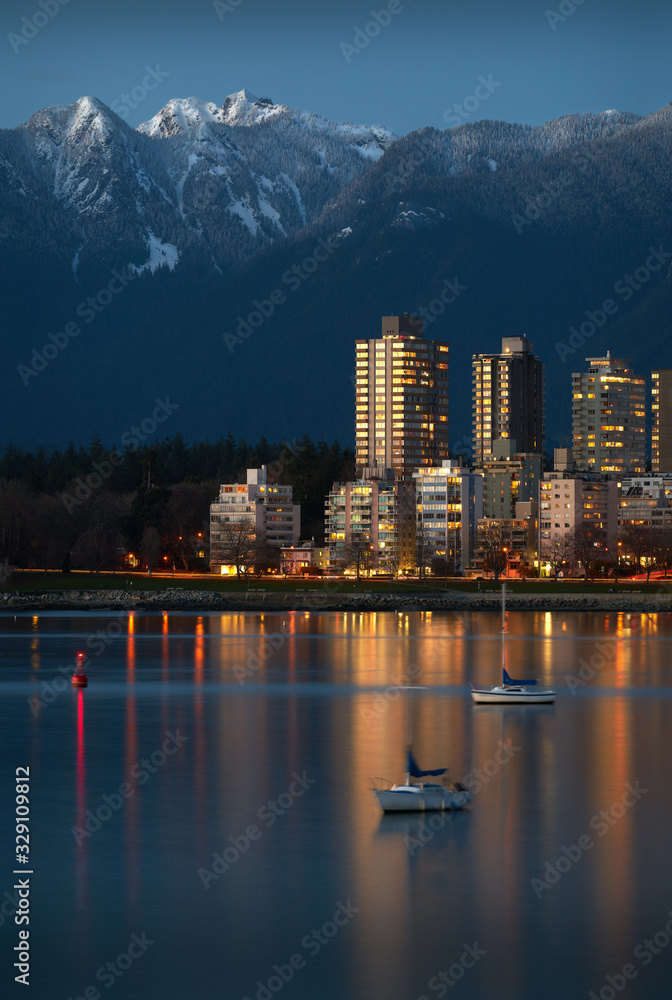 Fototapeta premium Vancouver West End Dusk. Sailboats anchored in English Bay. In the background are the snowcapped North Shore Mountains. Vancouver, British Columbia, Canada.